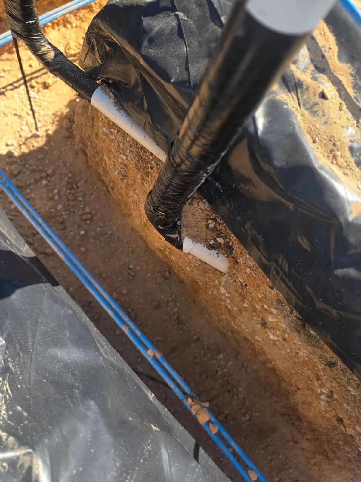 Wrapping ending at an exposed white pipe where it crosses a foundation trench
